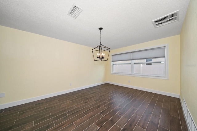 unfurnished dining area with a textured ceiling, dark hardwood / wood-style floors, and an inviting chandelier