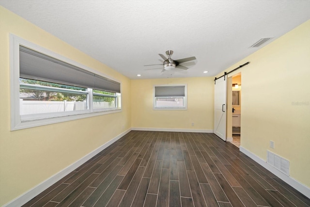 unfurnished room featuring a textured ceiling, a barn door, dark wood-type flooring, and ceiling fan