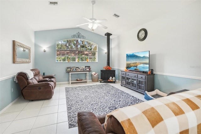 living room featuring light tile patterned floors, a wood stove, vaulted ceiling, and ceiling fan