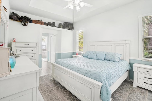 bedroom featuring light hardwood / wood-style flooring, ensuite bathroom, a raised ceiling, and ceiling fan