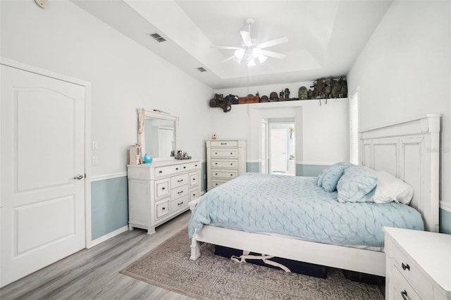 bedroom with light hardwood / wood-style flooring, a raised ceiling, and ceiling fan