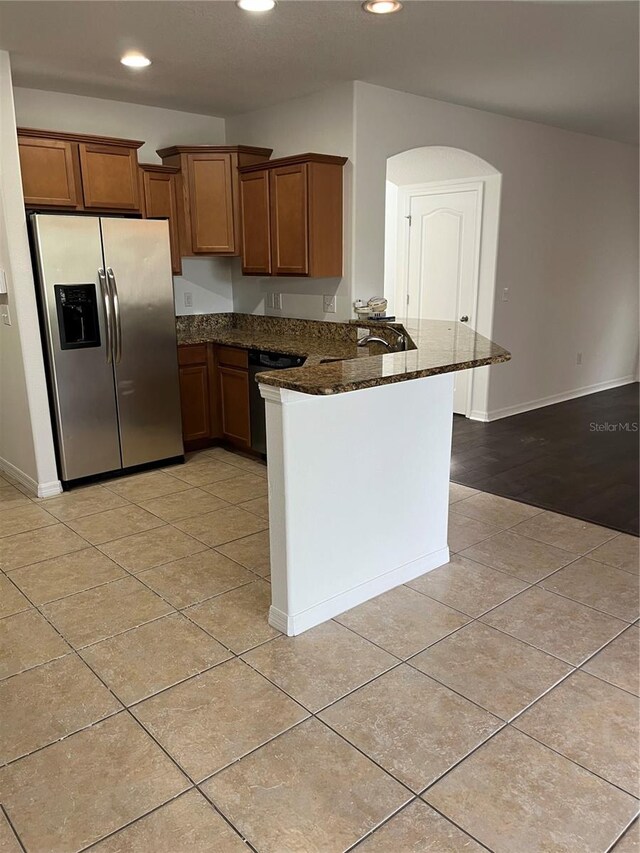 kitchen with dishwasher, stainless steel refrigerator with ice dispenser, dark stone countertops, light tile patterned floors, and kitchen peninsula