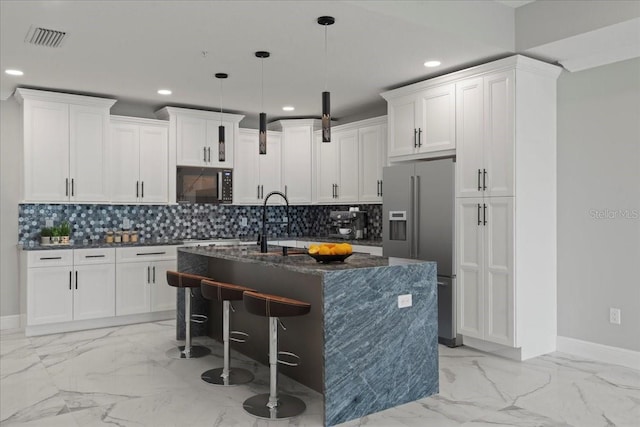 kitchen featuring high end refrigerator, a kitchen island with sink, white cabinets, and hanging light fixtures