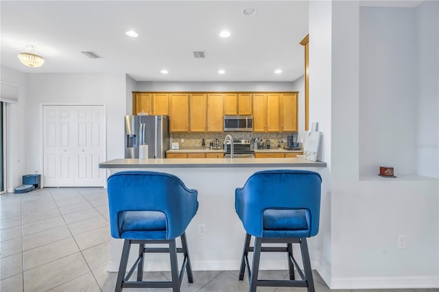 kitchen with brown cabinetry, stainless steel appliances, a peninsula, tasteful backsplash, and a kitchen bar