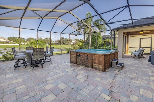view of patio with a water view, a lanai, outdoor dining area, and a hot tub