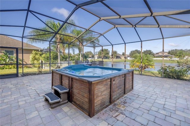 view of patio with a hot tub, a water view, and glass enclosure