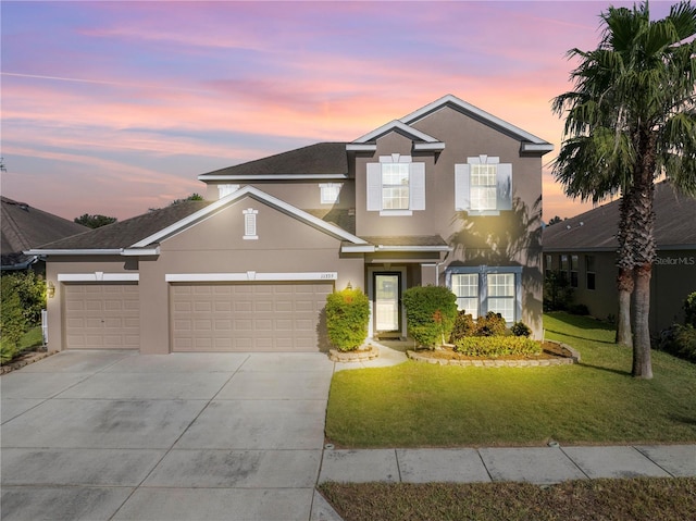 traditional-style house featuring an attached garage, stucco siding, concrete driveway, and a front yard