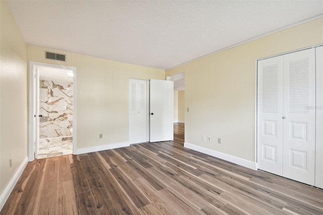 unfurnished bedroom with ensuite bathroom, wood-type flooring, and two closets