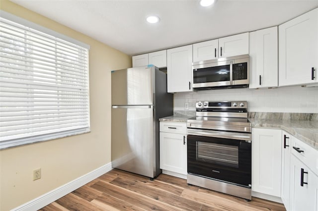 kitchen with appliances with stainless steel finishes, white cabinets, and light hardwood / wood-style floors