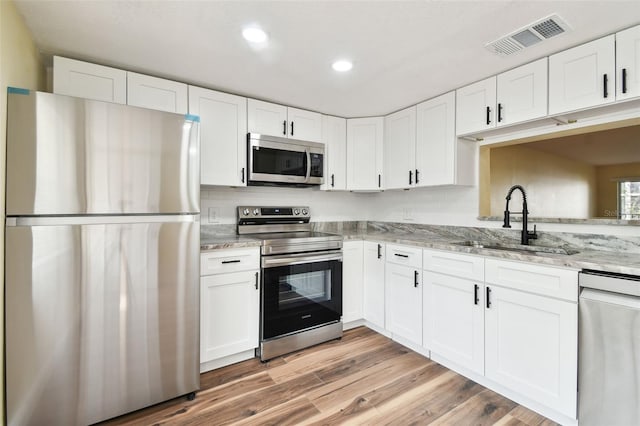 kitchen featuring sink, white cabinetry, stainless steel appliances, light stone counters, and light hardwood / wood-style flooring