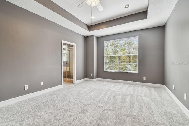 spare room with ceiling fan, a raised ceiling, and light carpet