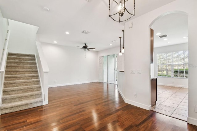 unfurnished room featuring visible vents, arched walkways, dark wood-style flooring, stairs, and ceiling fan with notable chandelier