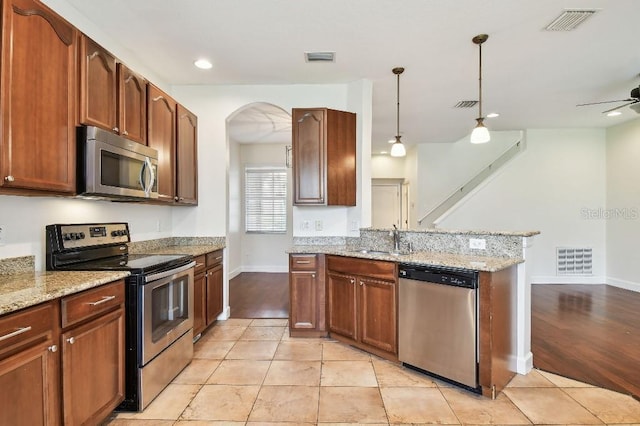 kitchen with stainless steel appliances, a sink, visible vents, light stone countertops, and decorative light fixtures