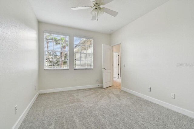 empty room featuring light carpet, a ceiling fan, and baseboards