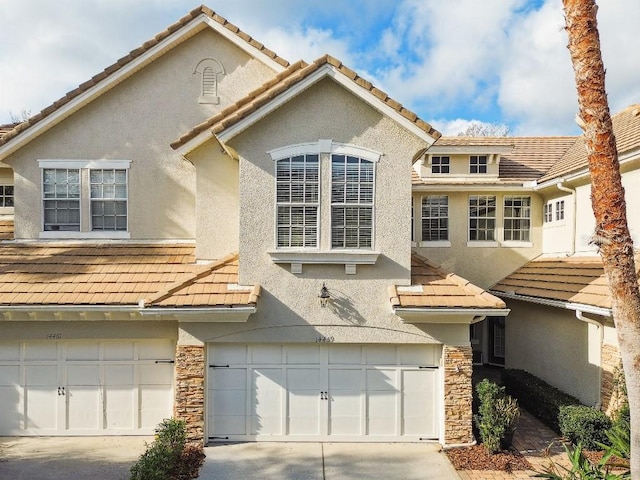 view of front of house with an attached garage, a tile roof, stone siding, concrete driveway, and stucco siding