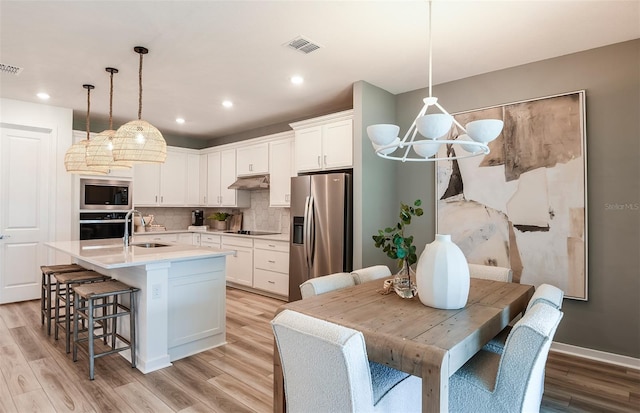 kitchen with appliances with stainless steel finishes, decorative light fixtures, a center island with sink, and light hardwood / wood-style flooring