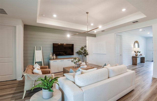 living room featuring wooden walls, a tray ceiling, and hardwood / wood-style floors