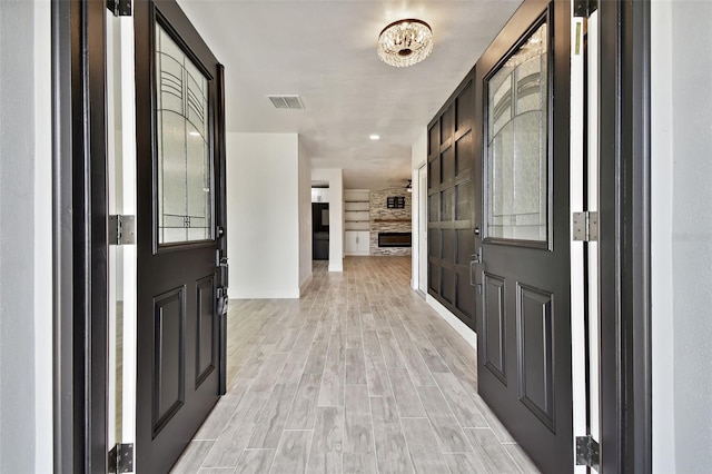 foyer entrance with a fireplace, light hardwood / wood-style floors, and an inviting chandelier