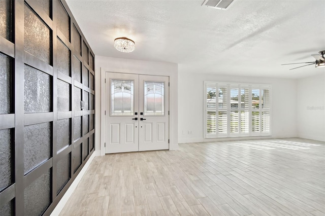 entryway with ceiling fan with notable chandelier, light wood-type flooring, a textured ceiling, and french doors