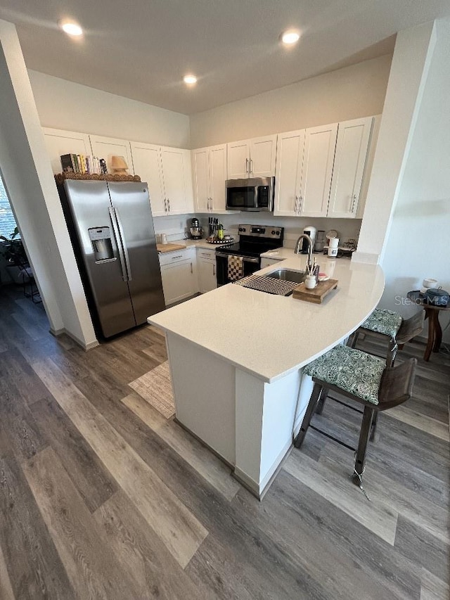 kitchen with white cabinetry, wood-type flooring, kitchen peninsula, and stainless steel appliances