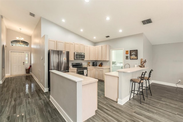 kitchen with kitchen peninsula, a breakfast bar area, appliances with stainless steel finishes, separate washer and dryer, and dark hardwood / wood-style floors