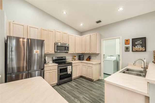 kitchen with stainless steel appliances, sink, vaulted ceiling, light wood-type flooring, and washer and dryer