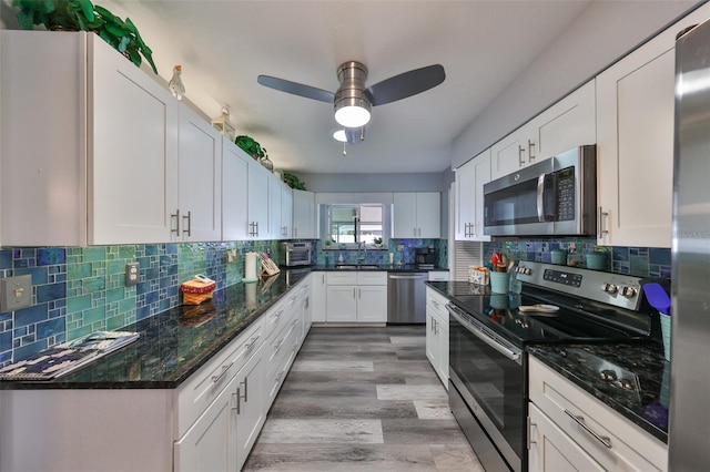 kitchen with white cabinetry, appliances with stainless steel finishes, dark stone counters, and light wood-type flooring