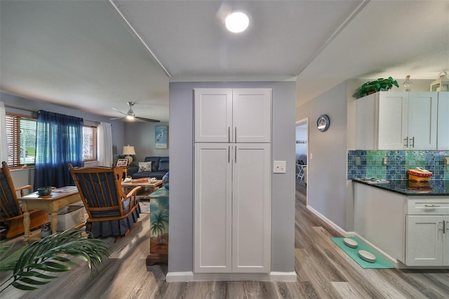 kitchen with tasteful backsplash, ceiling fan, white cabinetry, light wood-type flooring, and dark stone countertops