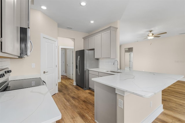 kitchen with kitchen peninsula, gray cabinetry, sink, appliances with stainless steel finishes, and light hardwood / wood-style floors