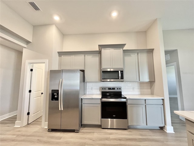 kitchen with gray cabinetry, decorative backsplash, light hardwood / wood-style flooring, and appliances with stainless steel finishes