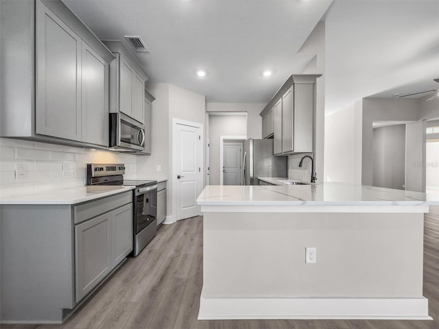 kitchen with sink, gray cabinetry, light hardwood / wood-style floors, kitchen peninsula, and stainless steel appliances