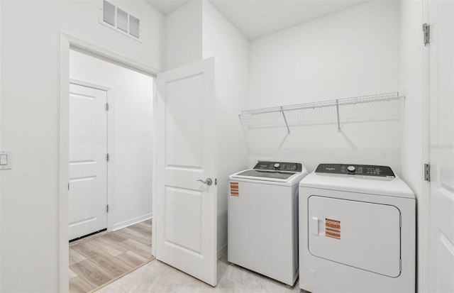 washroom with light wood-style flooring, laundry area, visible vents, baseboards, and washer and clothes dryer