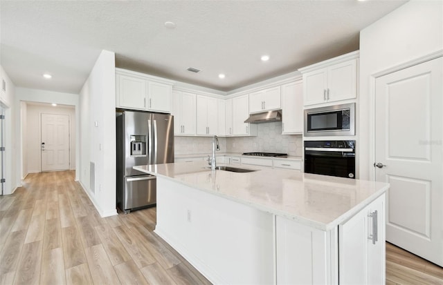 kitchen with an island with sink, appliances with stainless steel finishes, under cabinet range hood, white cabinetry, and a sink