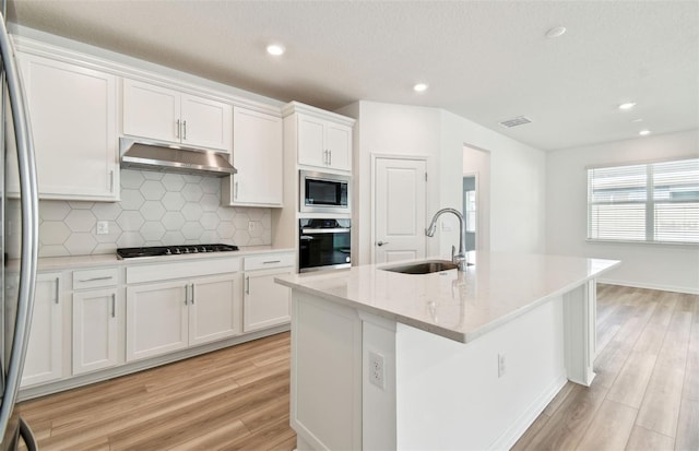 kitchen with a center island with sink, appliances with stainless steel finishes, under cabinet range hood, white cabinetry, and a sink