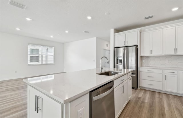 kitchen featuring stainless steel appliances, visible vents, white cabinets, a sink, and an island with sink