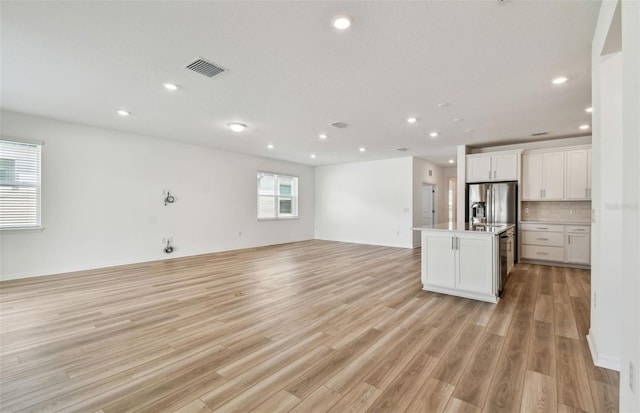 kitchen featuring visible vents, white cabinets, open floor plan, a kitchen island with sink, and stainless steel refrigerator with ice dispenser