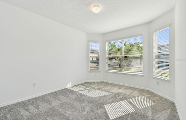 empty room with light carpet, a textured ceiling, and baseboards