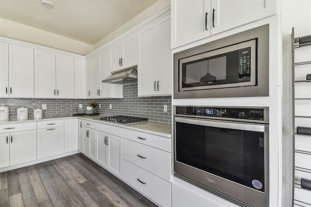 kitchen with tasteful backsplash, stainless steel appliances, white cabinets, dark wood-type flooring, and light stone counters