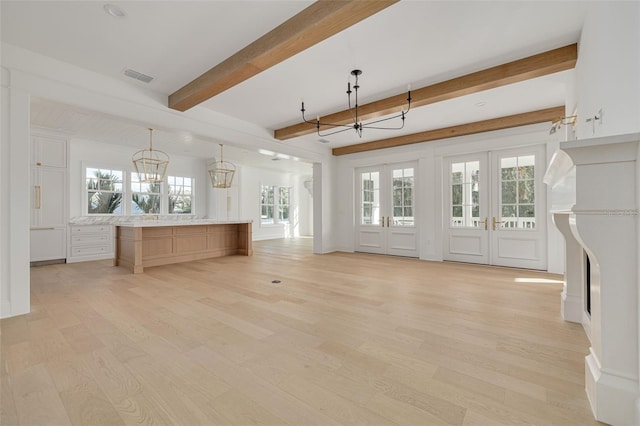 unfurnished living room with a notable chandelier, beamed ceiling, plenty of natural light, and light wood-type flooring