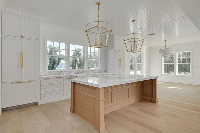 kitchen with hanging light fixtures, a spacious island, white cabinetry, light stone countertops, and light wood-type flooring