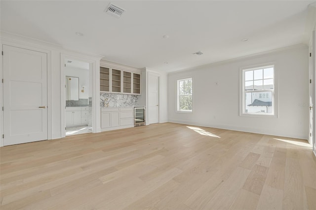 unfurnished living room with crown molding, light wood-type flooring, and beverage cooler