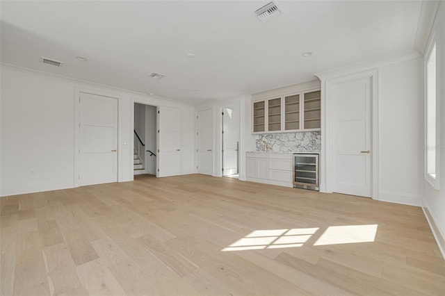 unfurnished living room featuring light hardwood / wood-style floors, bar, ornamental molding, and beverage cooler