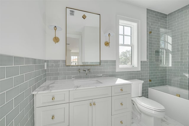 full bathroom with toilet, tiled shower / bath, vanity, and tile walls