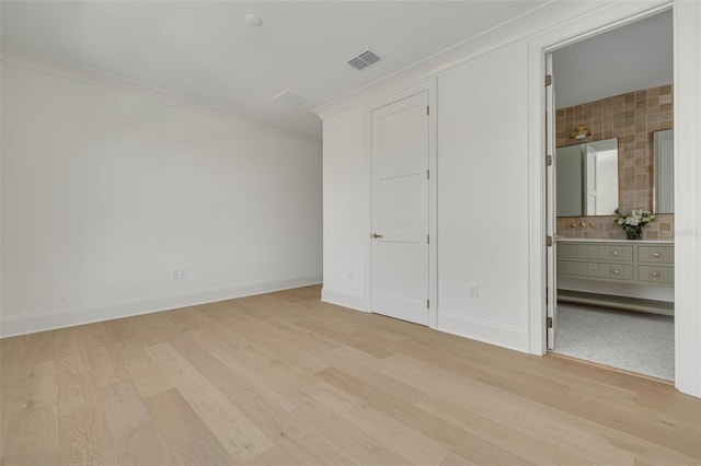 unfurnished bedroom with crown molding, ensuite bath, sink, and light wood-type flooring