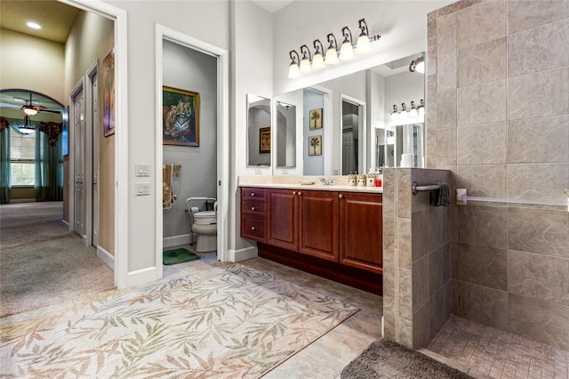 bathroom featuring vanity, toilet, a tile shower, and ceiling fan