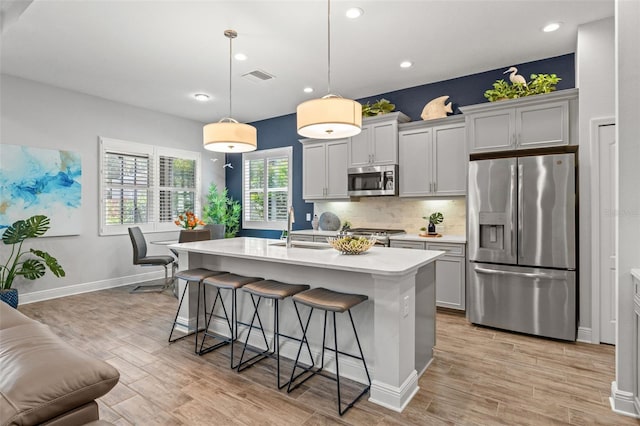 kitchen featuring stainless steel appliances, a kitchen island with sink, pendant lighting, and gray cabinets