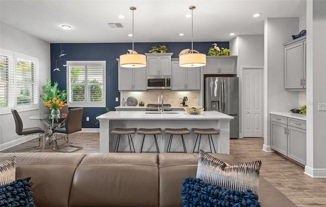 kitchen with a kitchen island with sink, appliances with stainless steel finishes, decorative light fixtures, and gray cabinets