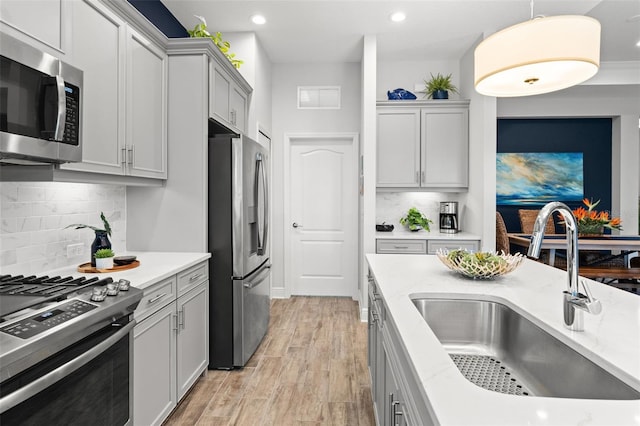 kitchen featuring decorative backsplash, sink, pendant lighting, light wood-type flooring, and appliances with stainless steel finishes