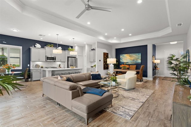 living room featuring sink, light hardwood / wood-style floors, a tray ceiling, and ceiling fan