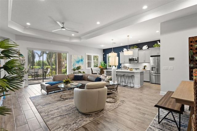 living room featuring ceiling fan, a tray ceiling, and light wood-type flooring